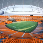 Render interior del Nou Mestalla del Valencia CF con las gradas naranjas en forma de bowl y la cubierta acristalada sobre el campo