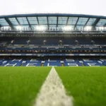 Vista interior del estadio Stamford Bridge, campo del Chelsea FC, con las gradas vacías y el césped iluminado antes de un partido