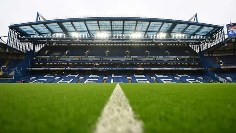 Vista interior del estadio Stamford Bridge, campo del Chelsea FC, con las gradas vacías y el césped iluminado antes de un partido