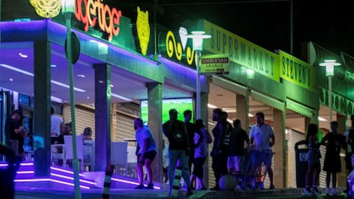 Turistas británicos en la zona de ocio nocturna de Benidorm durante el Mundial de Fútbol 2026, con neones y establecimientos de hostelería al fondo