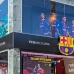 Fachada de la tienda oficial del FC Barcelona con el escudo del club y pantallas de campaña publicitaria