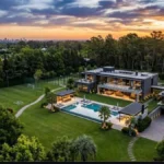 Vista aérea de una mansión de lujo con piscina, campo de fútbol y jardines al atardecer