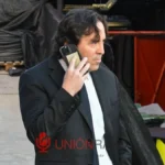 Raúl Martín Presa, presidente del Rayo Vallecano, habla por teléfono con traje negro en un entorno industrial