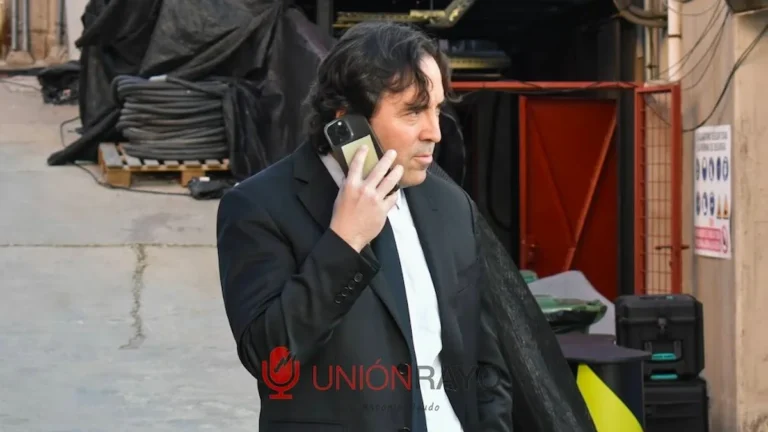Raúl Martín Presa, presidente del Rayo Vallecano, habla por teléfono con traje negro en un entorno industrial