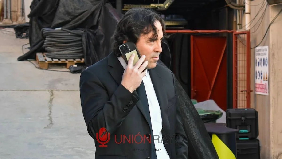 Raúl Martín Presa, presidente del Rayo Vallecano, habla por teléfono con traje negro en un entorno industrial