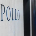 Cartel corporativo con el nombre Apollo grabado en la pared de un vestíbulo, con una persona desenfocada al fondo