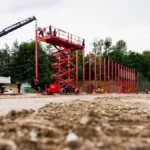 Operarios instalan postes rojos con una grúa y una plataforma elevadora en una obra deportiva