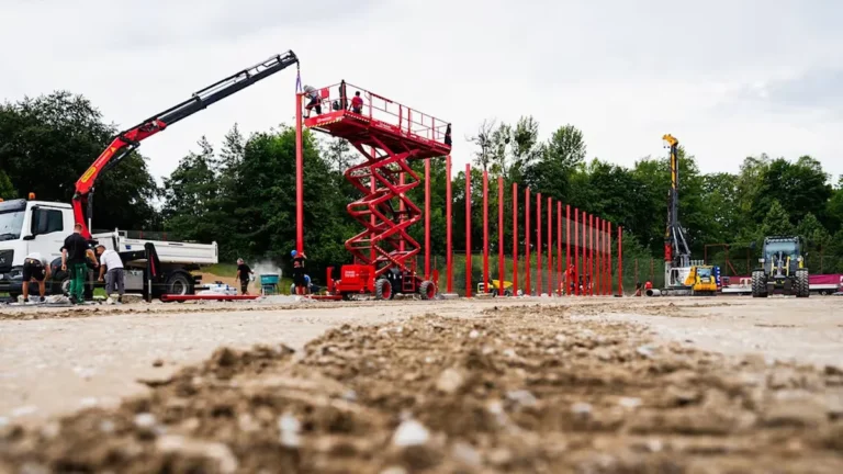Operarios instalan postes rojos con una grúa y una plataforma elevadora en una obra deportiva