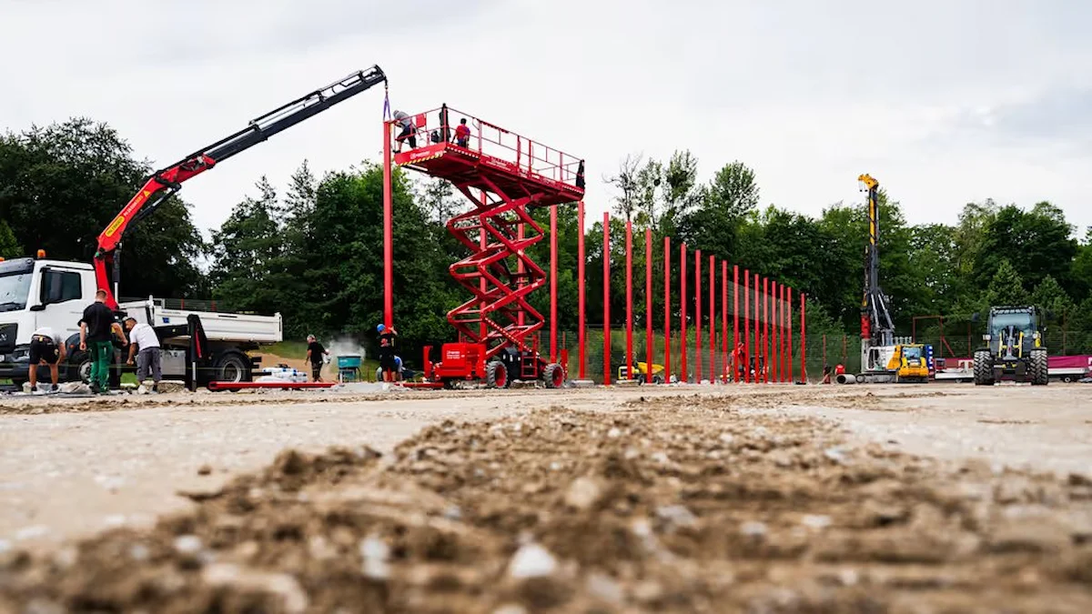 Operarios instalan postes rojos con una grúa y una plataforma elevadora en una obra deportiva