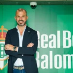 Directivo posa con brazos cruzados ante el escudo y la marca del Real Betis Balompié