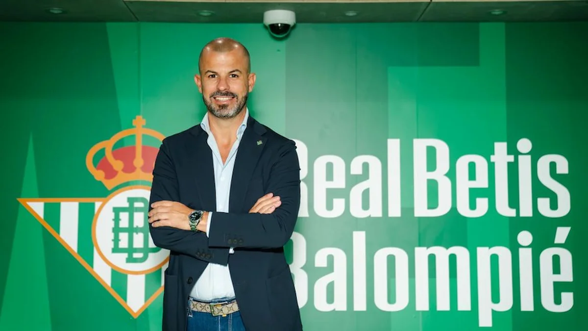 Directivo posa con brazos cruzados ante el escudo y la marca del Real Betis Balompié
