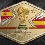Parche dorado con el trofeo del Mundial, dos estrellas y la leyenda de España campeona en 2010 y 2026