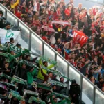 Aficionados del Real Betis y el Sevilla FC agitan bufandas en gradas separadas por una valla