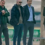 Cinco directivos conversan junto al césped durante un entrenamiento, con las gradas verdes al fondo