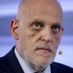 Directivo del fútbol profesional con traje oscuro y corbata granate escucha con gesto serio durante un acto institucional