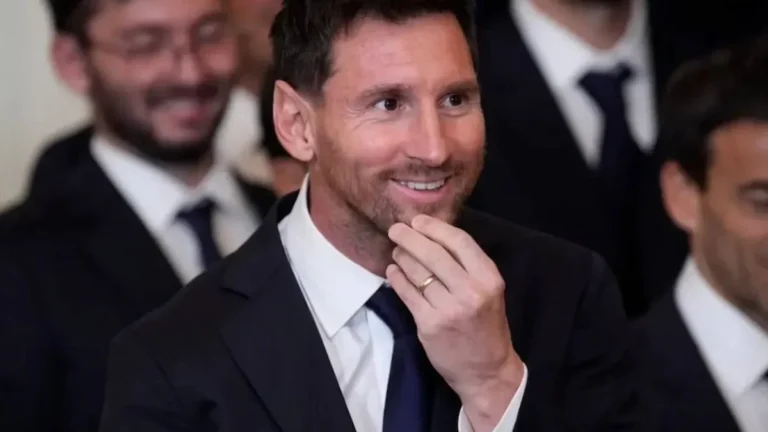 Leo Messi sonríe con gesto pensativo, con traje oscuro y corbata azul, durante un acto institucional